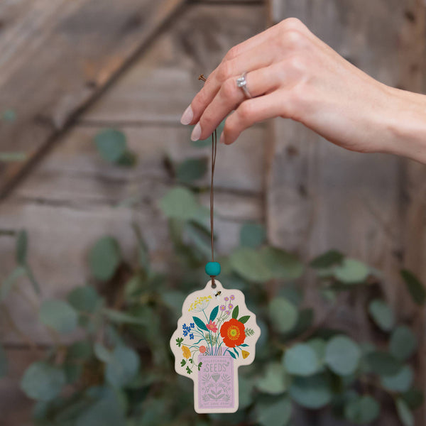 Hand holding a decorative hanging tag with floral design and text against a wooden background