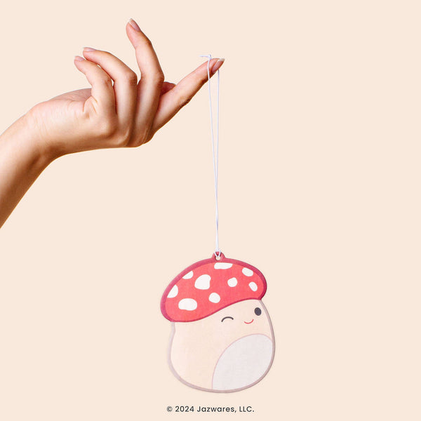 Hand holding a mushroom-shaped ornament with a smiley face on a beige background