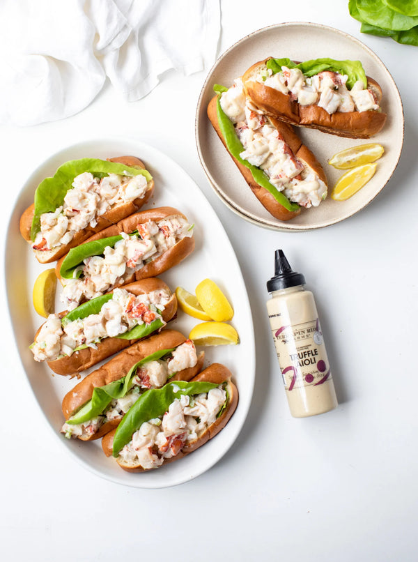 Plated seafood rolls with lemon wedges and a bottle of aioli on a white surface