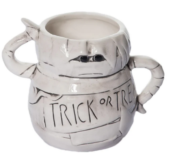 A ceramic mug with a white and gray color scheme, featuring text and a design that resembles a mummy's face.