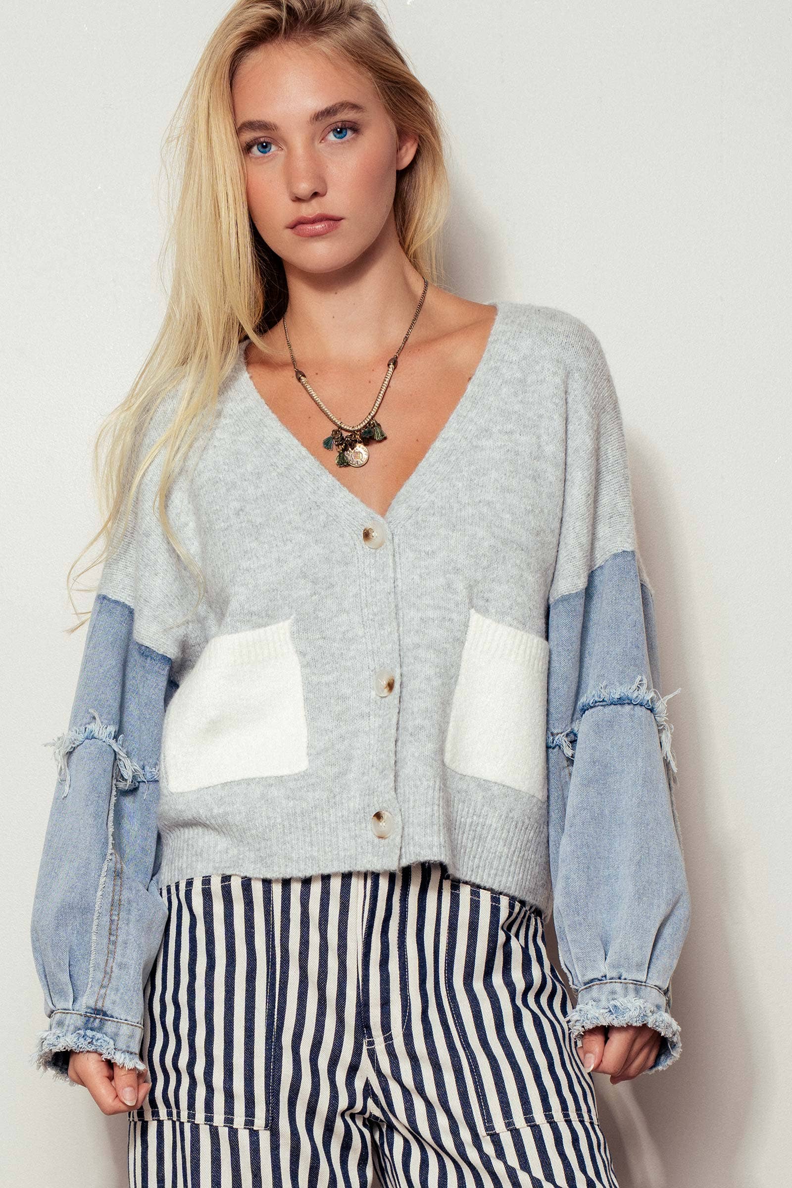 Woman wearing a patchwork cardigan with denim sleeves and striped pants against a white background