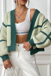 Person wearing a green and white striped cardigan over a white crop top and pants.