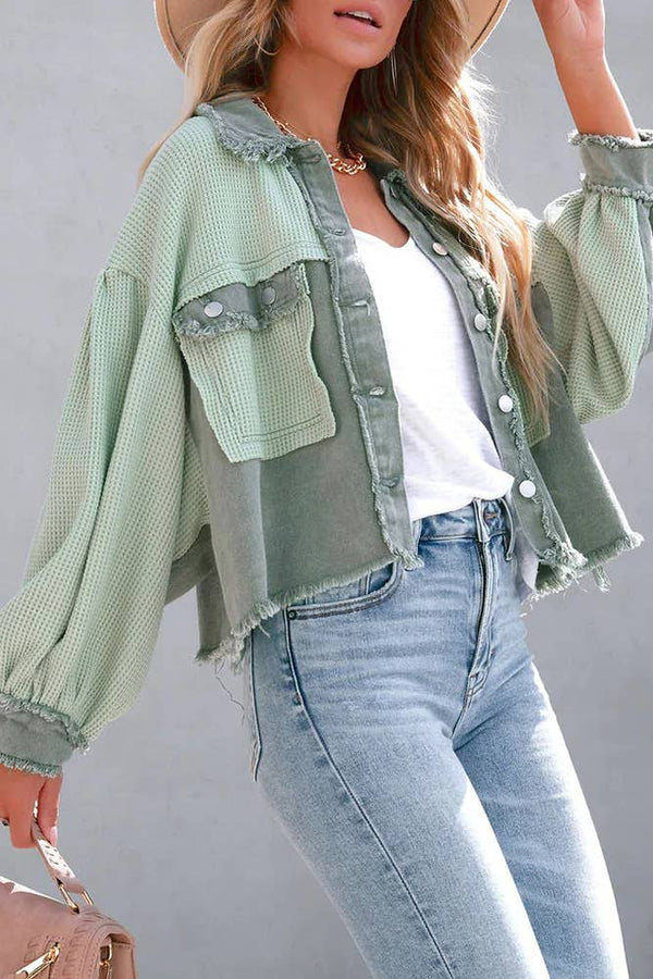 Woman wearing a light green denim jacket over a white top and blue jeans, standing against a gray background.