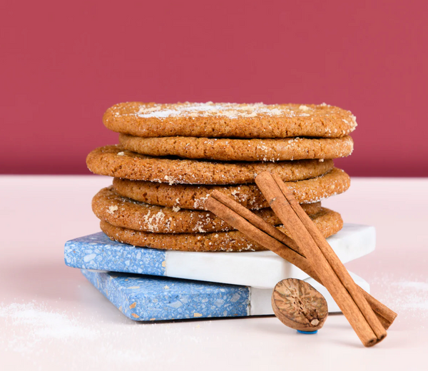 Stack of gingerbread cookies with cinnamon sticks on a white surface against a red background
