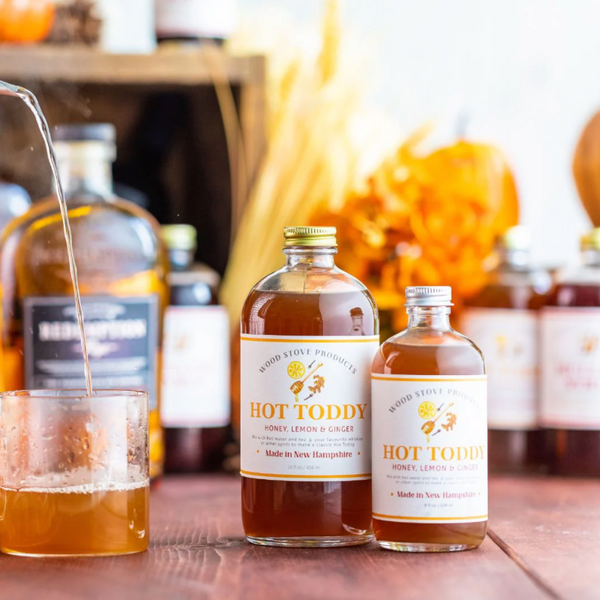Bottles of Wood Stove Products Hot Toddy on a wooden surface with a blurred background.