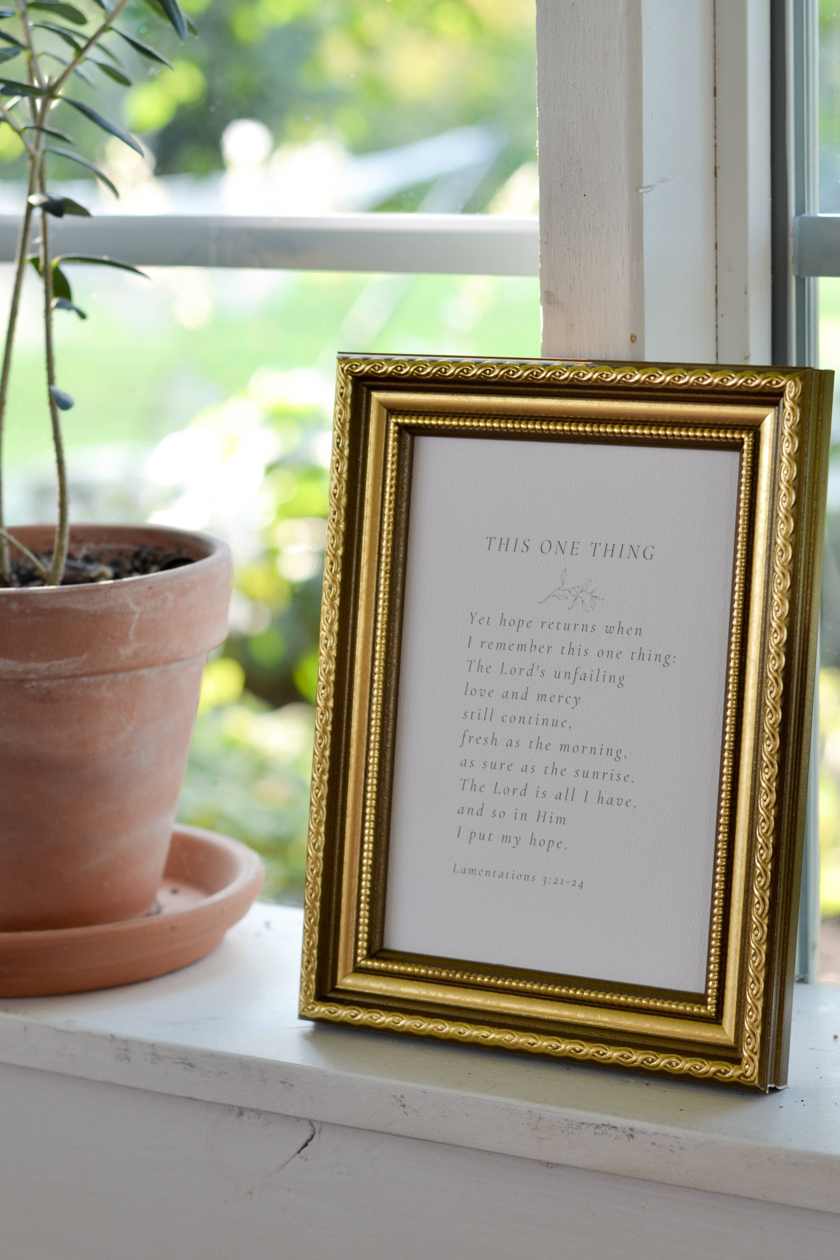 Gold-framed print with text on a windowsill next to a potted plant