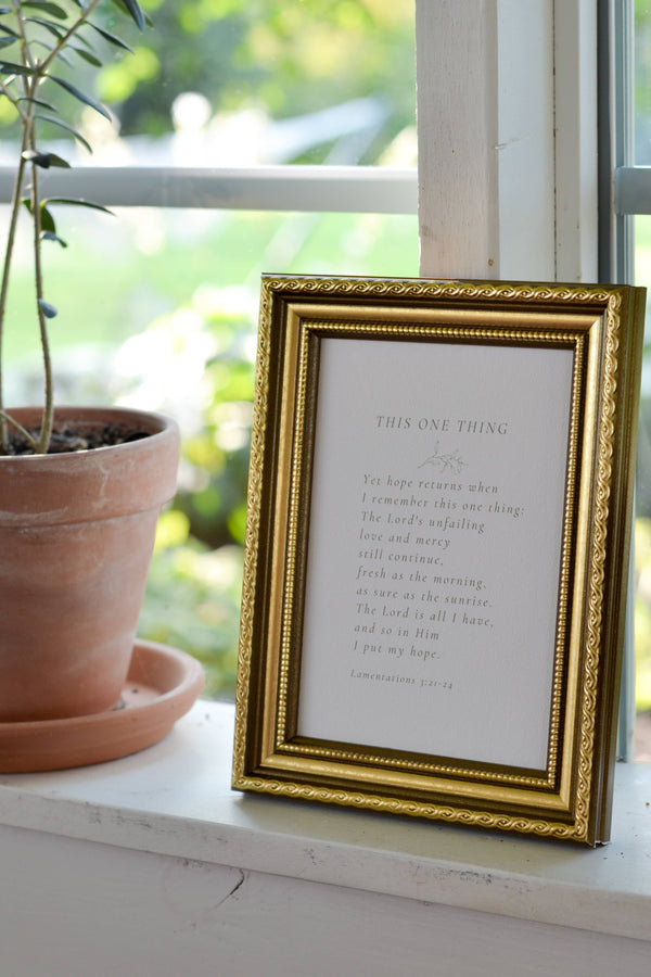 Gold-framed print with text on a windowsill next to a potted plant