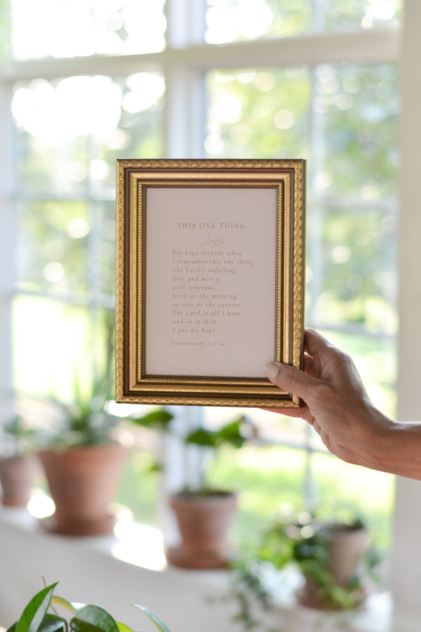 Hand holding a framed poem in front of a window with plants in the background