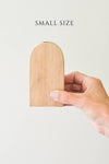 A small size wood arched bud vase held in a person's hand, with a beige color and a visible wood grain texture.