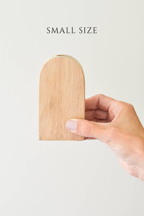 A small size wood arched bud vase held in a person's hand, with a beige color and a visible wood grain texture.