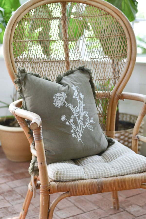 Wicker chair with a decorative pillow featuring floral design on a patio.