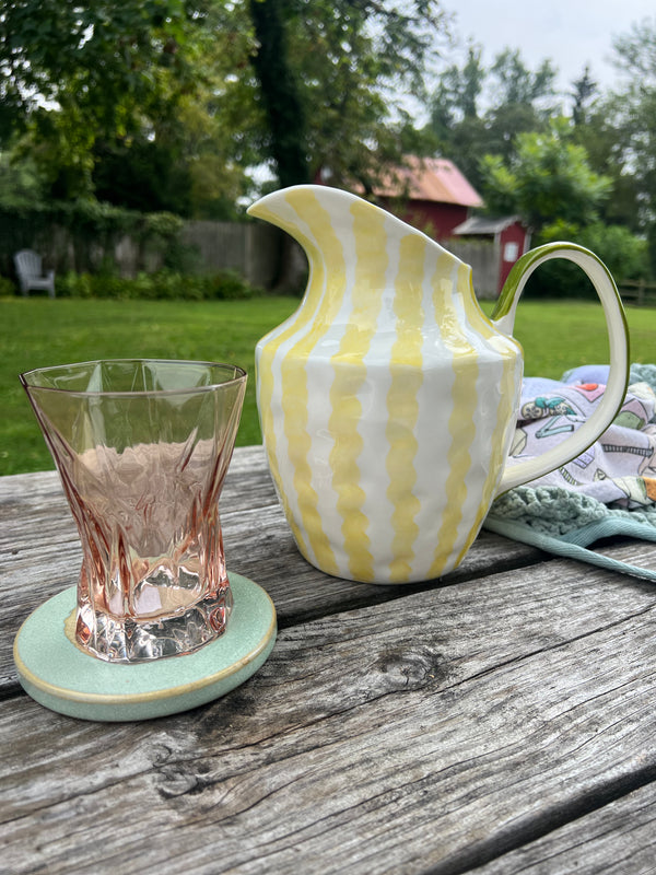 Yellow and white striped pitcher with a glass on a wooden surface outdoors