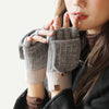 A close-up of a person wearing gray fingerless knit gloves with ribbed beige cuffs and a small brown button detail, against a soft light background.