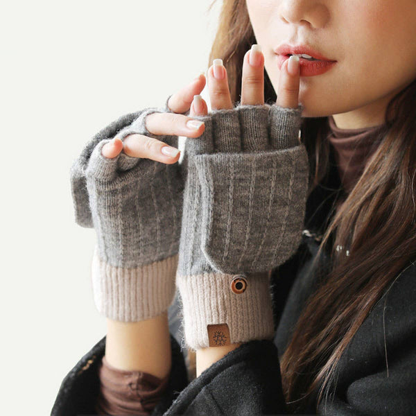 A close-up of a person wearing gray fingerless knit gloves with ribbed beige cuffs and a small brown button detail, against a soft light background.