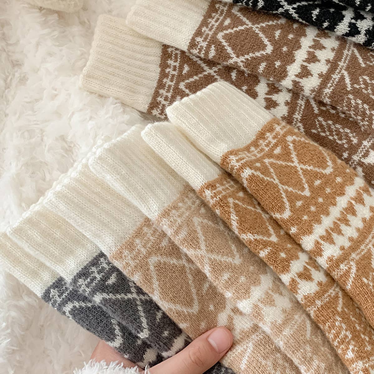 Stack of patterned socks with a hand holding them on a fluffy white surface