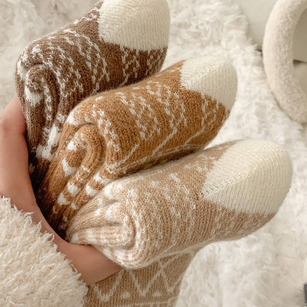 Pair of brown and white patterned socks held by a hand on a soft surface.