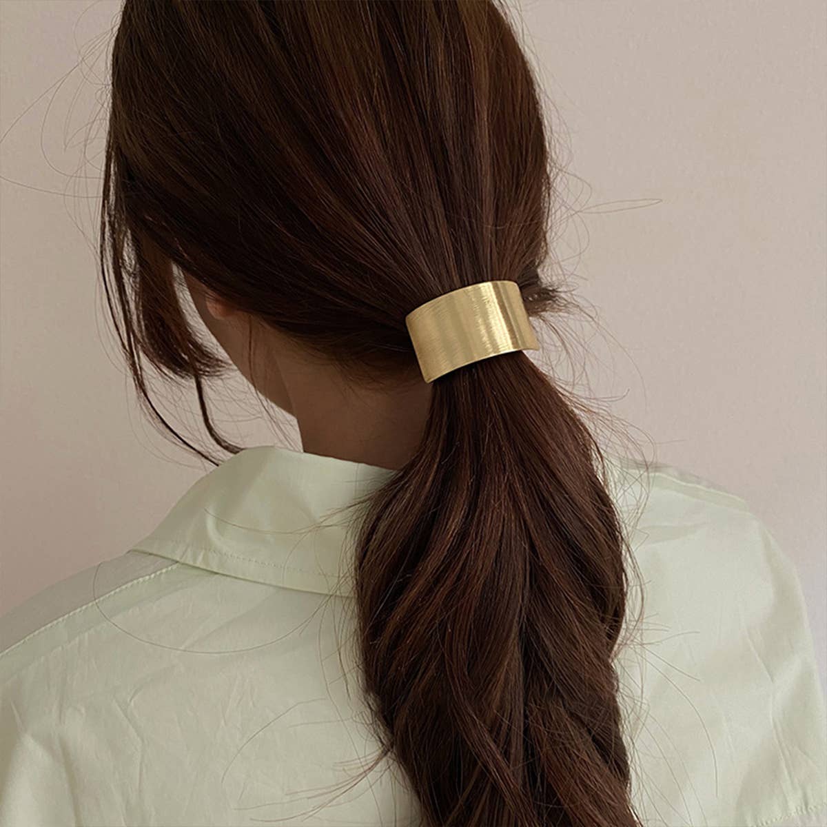 Person with a gold hair tie in a ponytail against a plain background