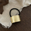 Black hair tie with a gold band on a textured fabric background