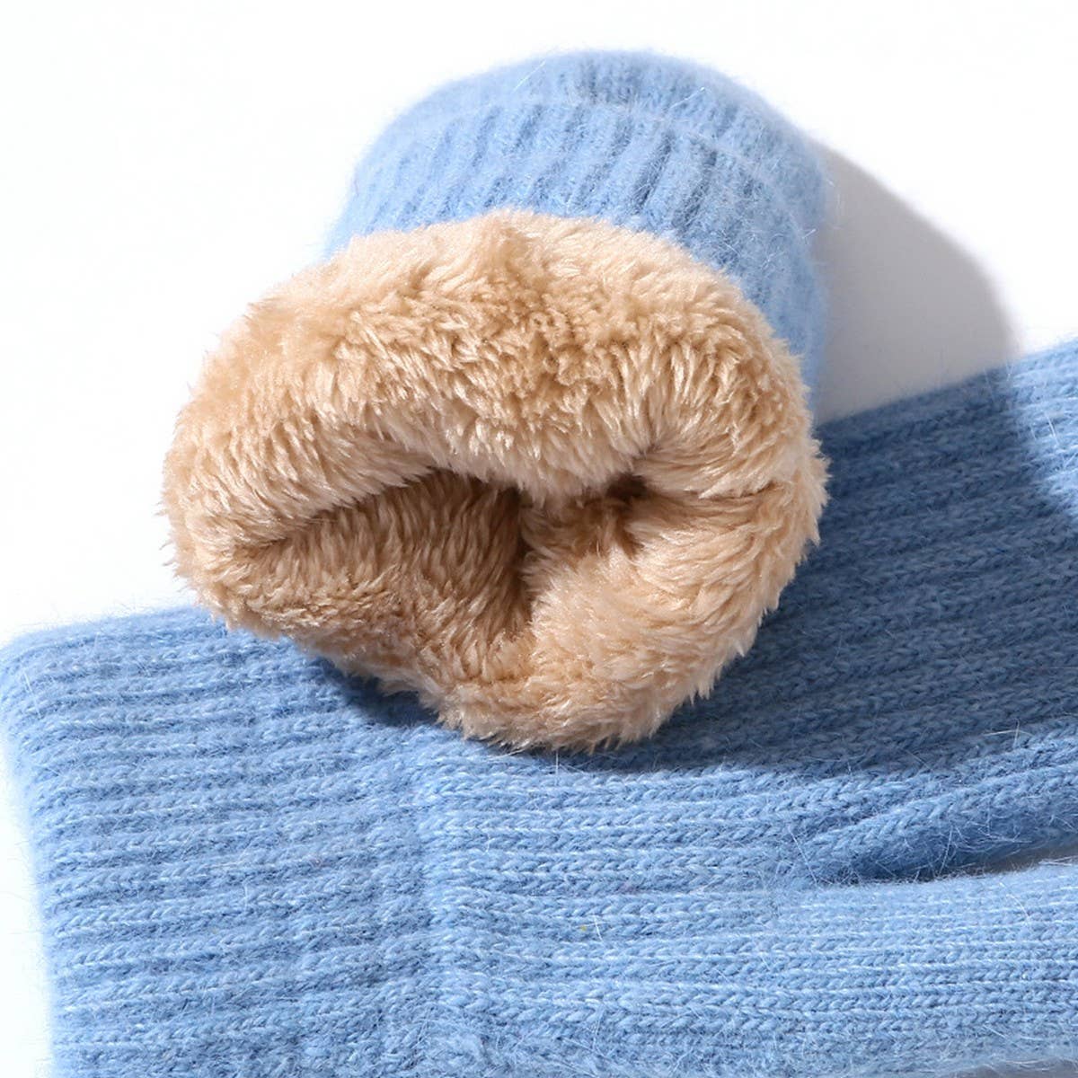 A close-up of a light blue ribbed knit beanie with a soft tan faux-fur lining rolled up at the brim, shown on a white background.