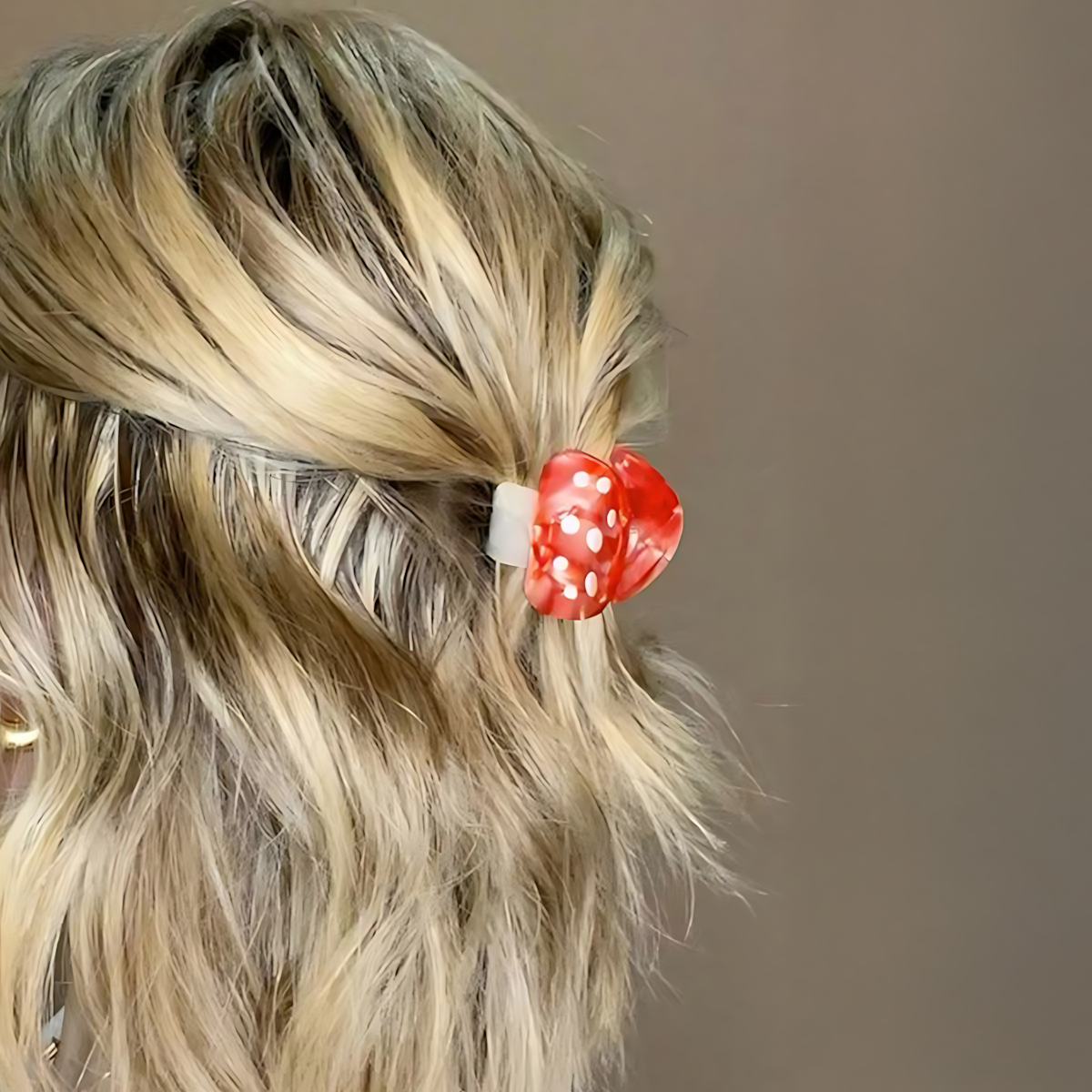 Blonde hair with a red polka dot hair clip against a neutral background