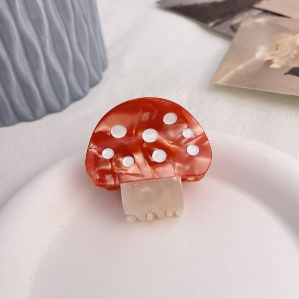 Mushroom-shaped hair clip with red cap and white spots on a light background