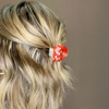 Blonde hair with a red polka dot hair clip against a neutral background