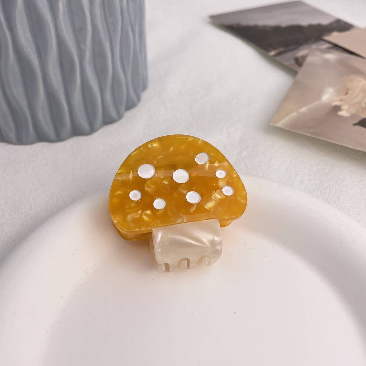 Mushroom-shaped hair clip with yellow cap and white spots on a light surface