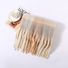 A soft rectangular scarf with fringe, laid flat on a white background. The scarf has a plaid-like block pattern in warm neutral tones, fading from beige and cream at the bottom into a lighter off-white at the top.