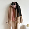A chunky knit scarf with fringe, draped over a cream coat. The scarf features a color-blocked pattern of dusty pink, dark charcoal gray, and a heathered beige-and-gray mix.