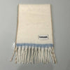 An off-white wool scarf with a light blue horizontal stripe and fringe, featuring a 'FUNFUNGRL' brand label, laid flat on a gray background.