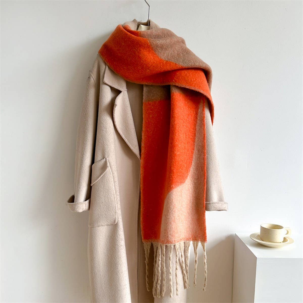 Beige coat with a red and beige scarf draped over it on a white background