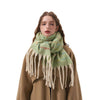 A woman wearing a light green and cream plaid fringed scarf with a brown coat, photographed against a solid white background.