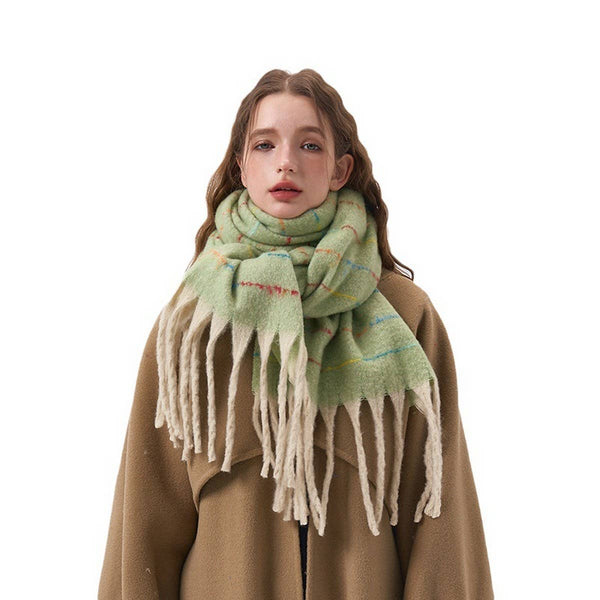 A woman wearing a light green and cream plaid fringed scarf with a brown coat, photographed against a solid white background.