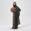 A woman models a long, double-layered wrap coat featuring a solid camel brown side and a textured multicolor tweed patterned side with cream fringe, worn over a black turtleneck against a plain white studio background.