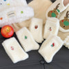 White fluffy phone cases with embroidered designs on a dark surface.