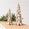 Two decorative metallic gold Christmas tree ornaments of different sizes displayed on a wooden table with green pine branches in the background.