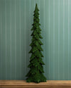 A dark green pine tree Christmas tree ornament or decorative figurine standing on a wooden surface against a teal-green vertical beadboard wall.