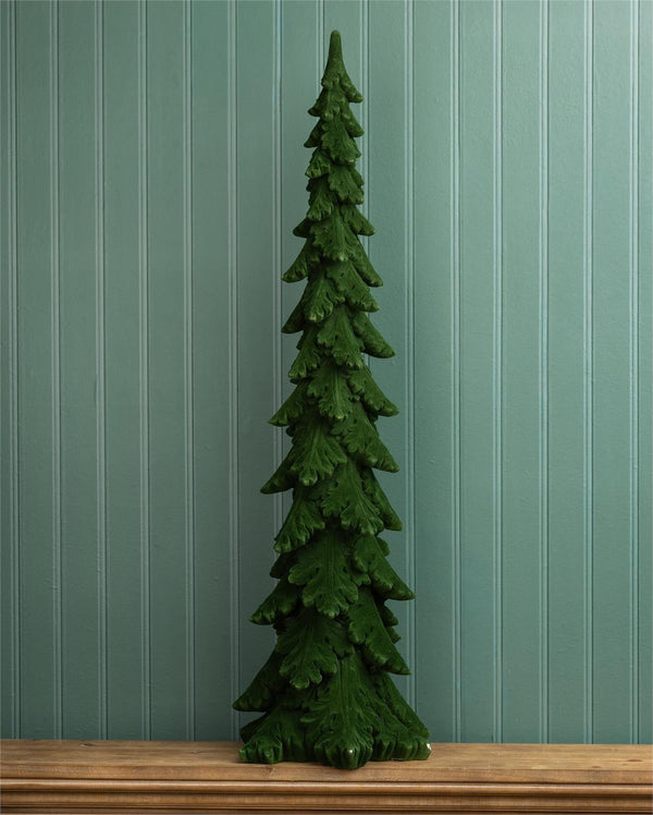 A dark green pine tree Christmas tree ornament or decorative figurine standing on a wooden surface against a teal-green vertical beadboard wall.