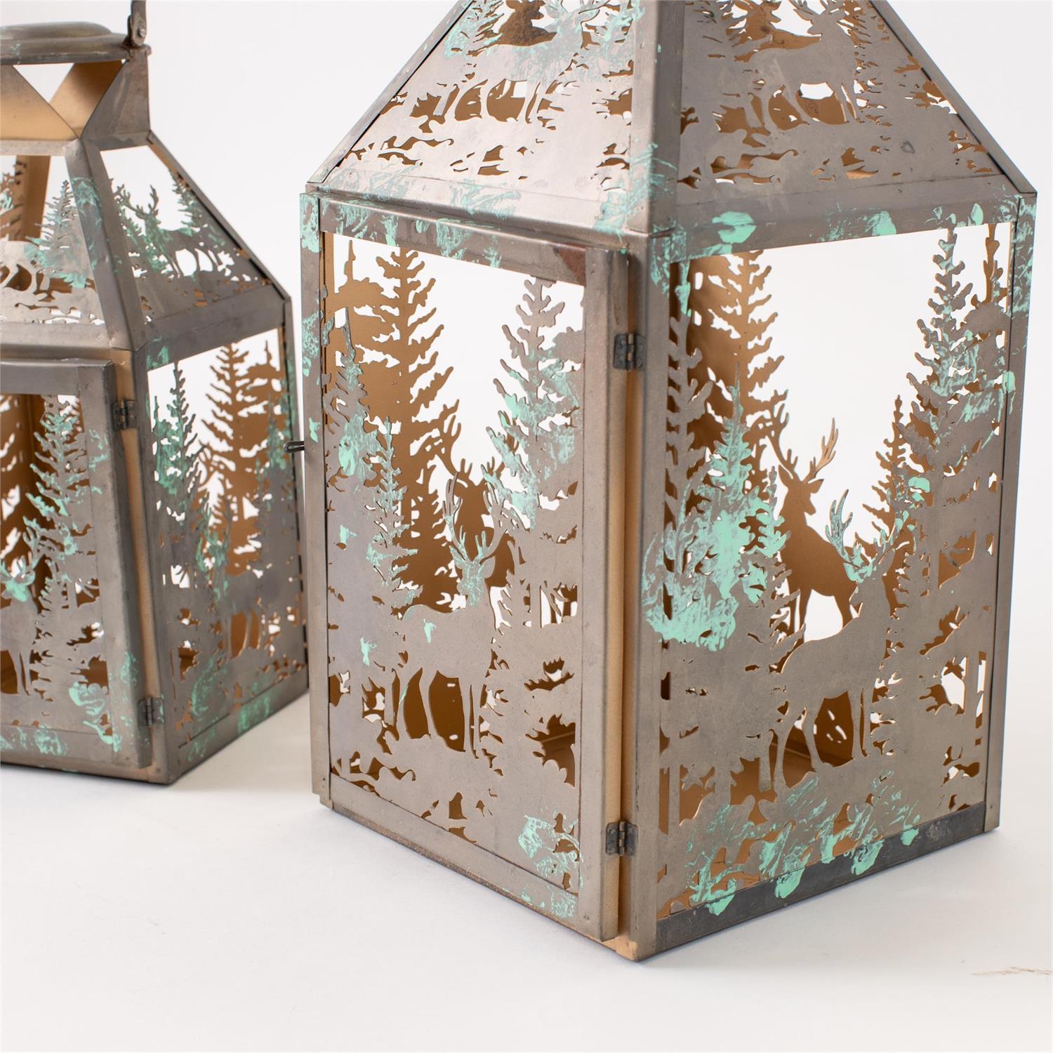 Decorative metal lanterns with a forest silhouette cutout design, featuring a weathered bronze finish with distressed turquoise patina accents, shown on a white background.