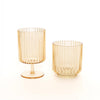 Two amber-colored ribbed glass tumblers, one with a stem and base and one shorter tumbler, on a clean white background.