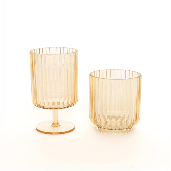 Two amber-colored ribbed glass tumblers, one with a stem and base and one shorter tumbler, on a clean white background.