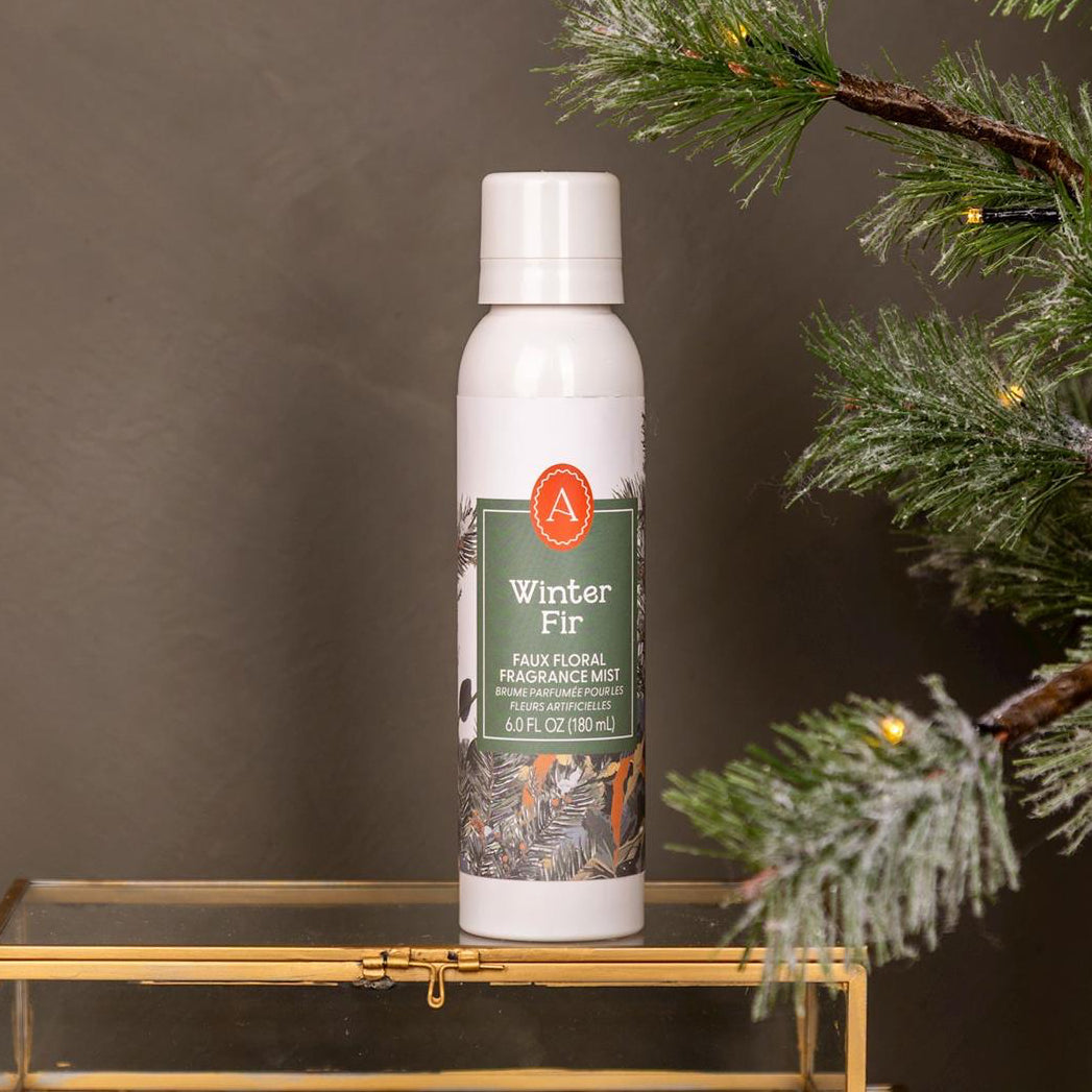 White spray bottle labeled 'Winter Fit' on a gold stand with a Christmas tree in the background