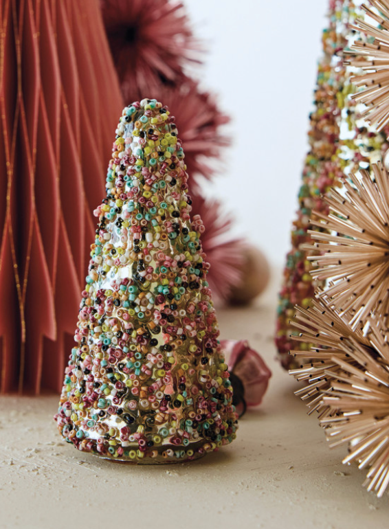 A small cone-shaped decorative tree covered in multicolored sequins, styled on a tabletop with other festive decor in the background.