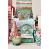 A collection of vintage Christmas-themed decorative items, including a green and red 'Books' book-shaped ornament, a pink glittery Christmas tree, a green glass candle holder, and a snow globe with a miniature Christmas village scene on an open book.