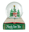 A Christmas-themed snow globe figurine resting on an open book base. The clear globe contains a miniature winter scene with green Christmas trees, a small house, snow, and a gold star.