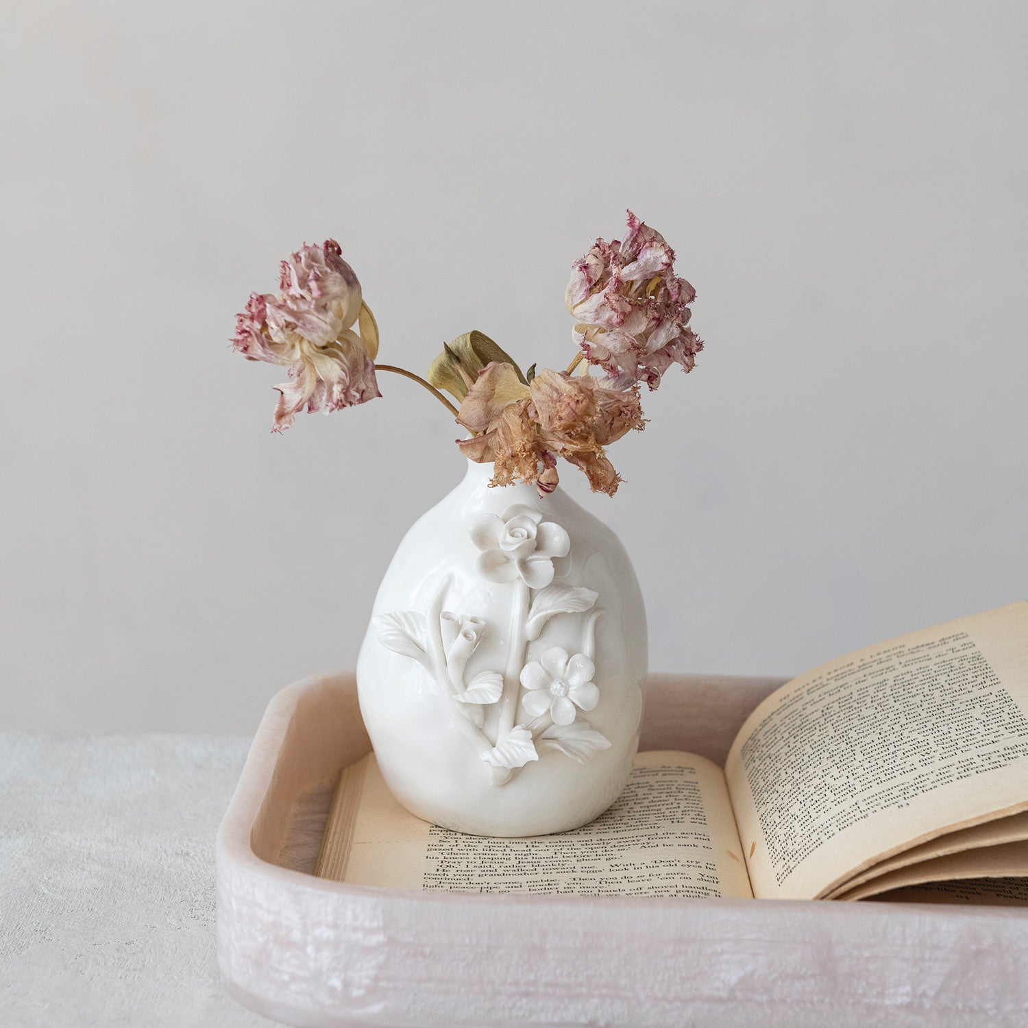 White decorative vase with floral patterns on a tray with an open book