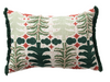 A rectangular decorative throw pillow with a festive embroidered pattern of pine trees, stars, and clouds in green and red on a cream linen background, finished with dark green fringe on the sides.