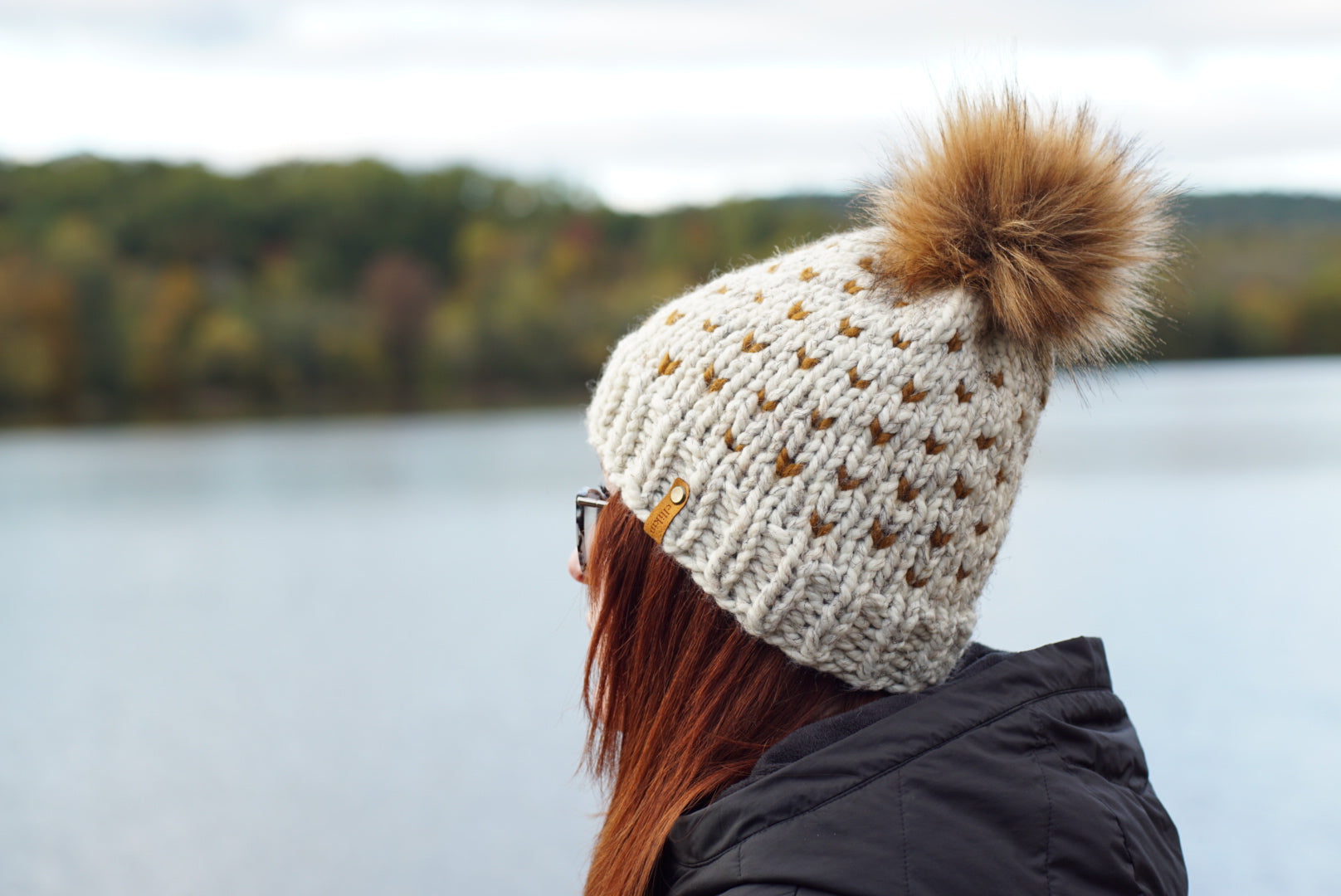 Person wearing a knitted hat with a pom-pom by a lake