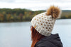 Person wearing a knitted hat with a pom-pom by a lake