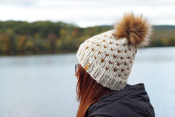 Person wearing a knitted hat with a pom-pom by a lake